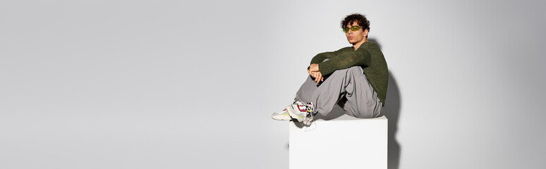 Stylish curly man confidently poses in trendy outfit against a minimalist backdrop