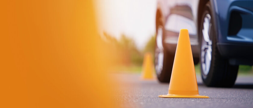 Orange traffic cones with blurred car in background asphalt road banner, driving school practice area, safe driving lessons, vehicle maneuvering skills, practical driving test preparation copy space