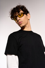 Obraz premium Stylish man wearing sunglasses showcases trendy fashion in a modern studio setting