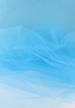 Bright blue tulle fabric on blue background.  Abstract transparent material curve wave.
