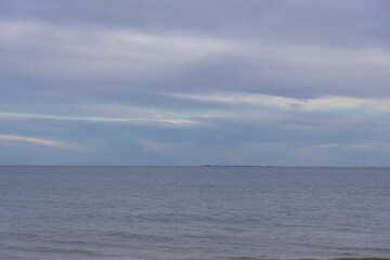 Obraz premium the calm sea under a soft cloudy sky over a distant shore evokes tranquility and serenity, capturing a peaceful moment by the water with gentle waves