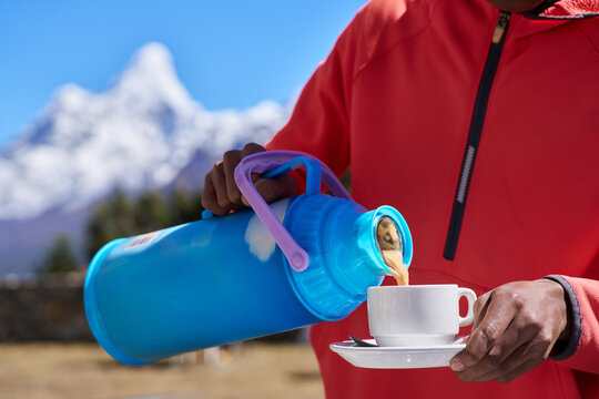 Coffee with view of Amadablam: Traveler's hand in fleece jacket pours hot coffee from thermos into mug against majestic backdrop of Amadablam peak during rest break on Everest Base Camp trek, Nepal.