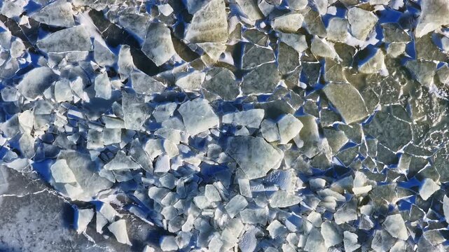 Fractured ice covering frozen sea surface, creating patterns of cold and winter environment in aerial top down view