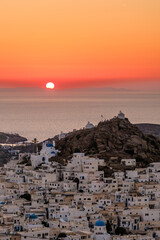 Panoramic view of the beautiful whitewashed village also known as chora, in Ios Greece, and a spectacular orange sunset in the background