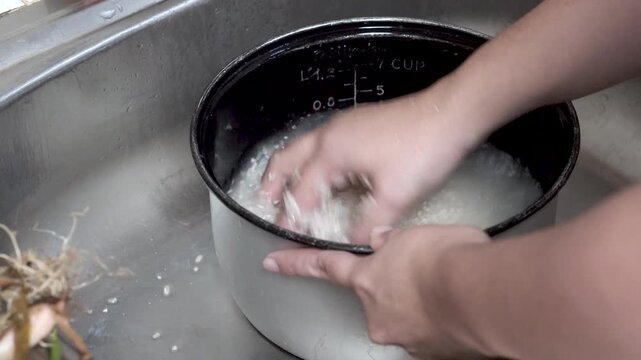 Close-up image of hands washing rice in a pot. The rice, which will be cooked into rice, is washed to remove any remaining dirt.
