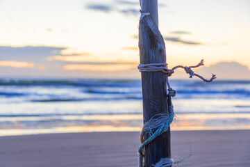 A rustic wooden post tied with rope stands on sandy beach at sunset near Mediterranean sea in Spain, evoking calm and tranquility. © alma.photo