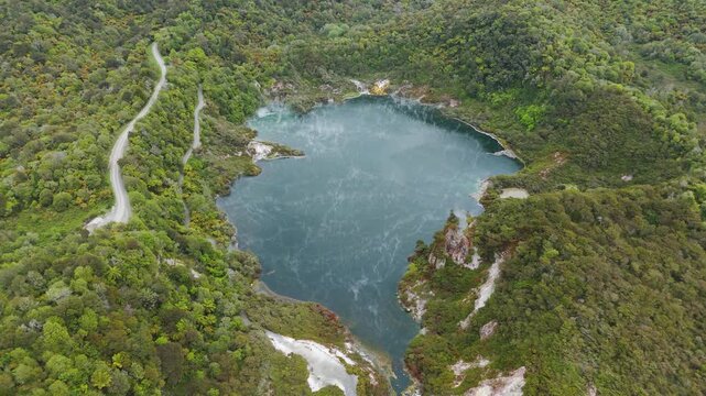Frying Pan Lake steams in Waimangu Volcanic Valley near Rotorua, wide left orbit drone shot.