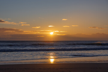 Obraz premium A golden sunset over the Mediterranean Sea in Spain, capturing a serene beach scene with waves gently lapping at the shore, perfect for a tranquil