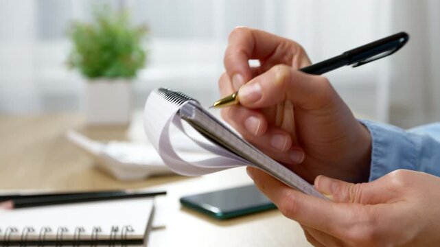 Close-up of a woman's hand writing in a notebook on a desk. Concept of business planning, management, and taking notes.