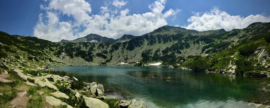A panorama view of the peaks of the Pirin mountain in Bulgaria - a snow fed lake on high ground in the mountain is clear and beautiful on a sunny day