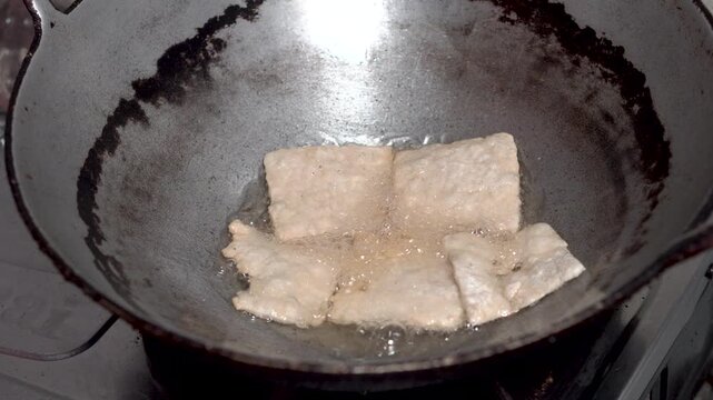Fried tempeh coated in flour, fried in hot oil in a pan. Close-up of nearly cooked tempeh.