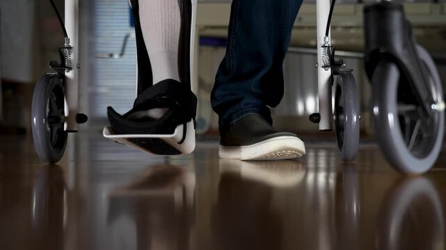 Person in Leg Brace Using a Walker for Rehabilitation. Close-up of a person wearing a medical walking boot and using a rolling walker for mobility and recovery in a home or hospital setting