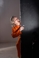 Escape attempt of a prisoner in orange jumpsuit. Man in shadow looking back with fear during a jailbreak. Cinematic crime and justice concept.