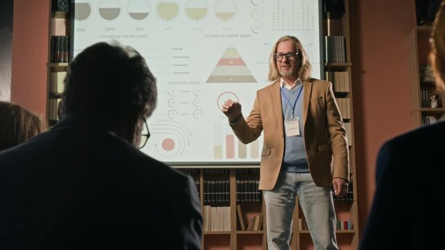 Low angle shot of passionate middle-aged Caucasian man with long blonde hair and beard delivering presentation on stage