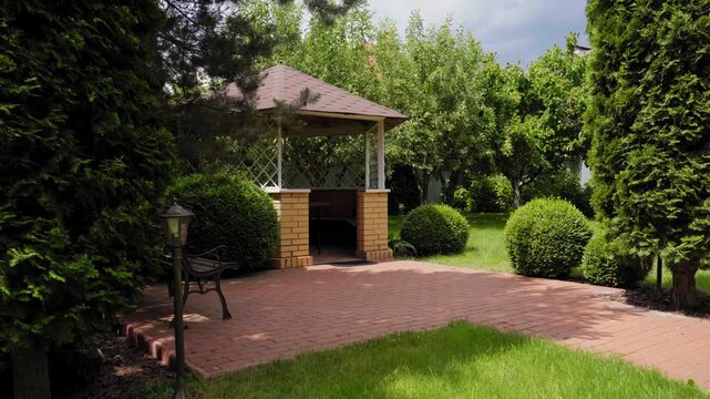 Cozy garden gazebo with brick patio and manicured shrubs, peaceful backyard landscape with green lawn and trees