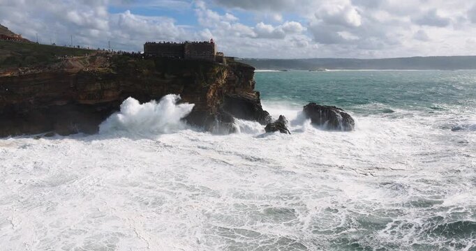 High drone shot of Nazar&eacute; cliffs with turbulent Atlantic swell surging toward rocky shoreline