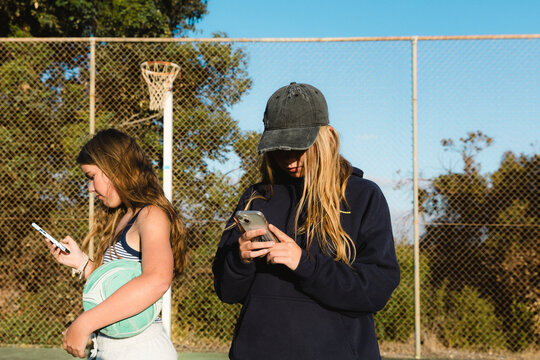 Close up of two teenage girls on smart phones holding ball at outdoor court