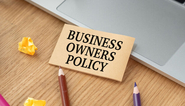 Business Owners Policy (BOP) text on a craft card on a wooden desk with a laptop and pencils.
