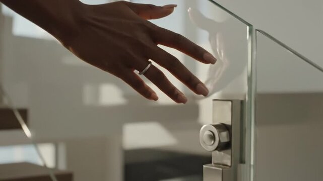 Hand in soft focus opening modern glass door with sleek silver handle, capturing a serene moment in a minimalist interior, warm natural light, and tranquil atmosphere, in a contemporary arch