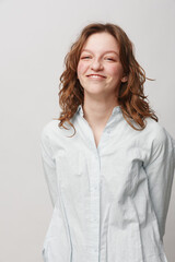 Obraz premium Smiling young woman with curly hair wearing a white shirt stands against a light background. She looks confident and happy, expressing natural beauty and casual style.