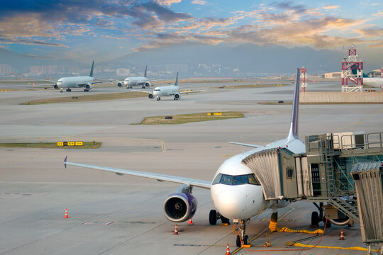 Aircraft at the jet bridge is preparing for takeoff, while in the distance three other passenger jetliners are taxiing for takeoff and landing in the evening with a beautiful sky, sunset, and sunrise.