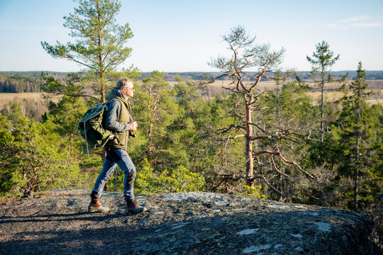 Male hiker taking photos with vintage camera on scenic cliff in Finland. Travel photography, adventure tourism and outdoor lifestyle concept.