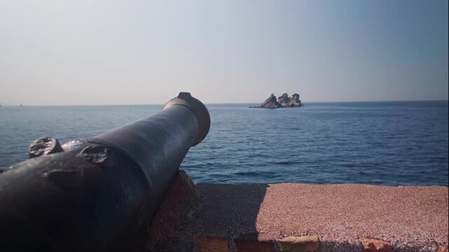 Panoramic view of historic iron cannon on Petrovac waterfront pointing to sea with calm blue waters in background