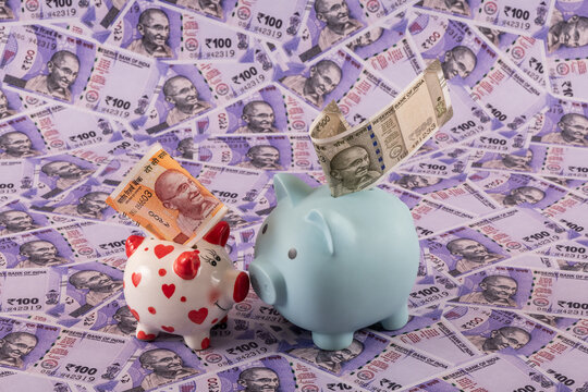 Two piggy banks against a background of Indian rupees