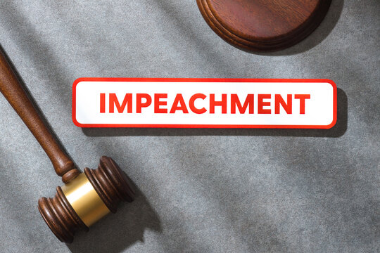 A judge&rsquo;s gavel next to a red &ldquo;IMPEACHMENT&rdquo; sign on gray stone textured surface in soft sunlight, symbolizing political accountability and legal proceedings. Top view.