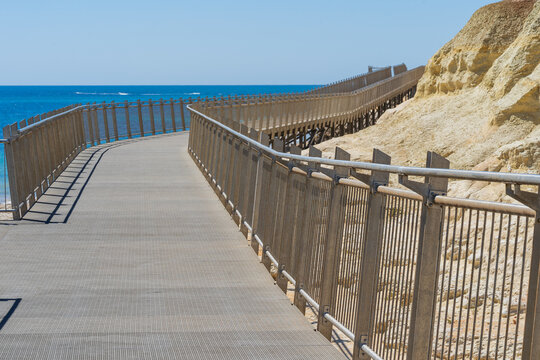 A fenced boardwalk made of steel winding away toward a distant blue ocean