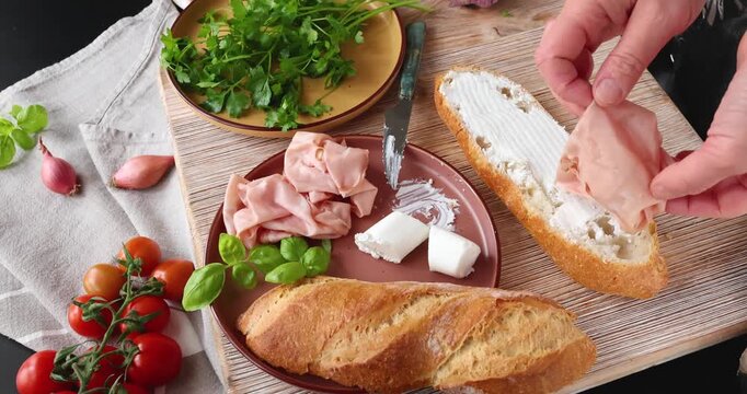 Anonymous person prepares sandwich with cheese, basil, and mortadella in kitchen. Italian cuisine, high-quality farm-to-table ingredients.
