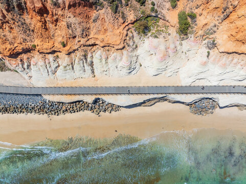 Aerial view of a walkway along a rugged eroded coastline and beach below