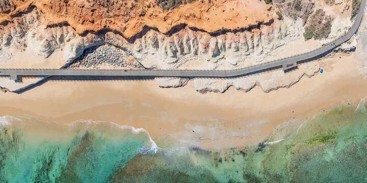 Aerial view of a walkway along a rugged eroded coastline and beach below