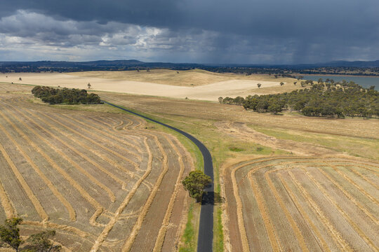 Aerial view of dark clouds and rain over a bend in a country road running through harvested farmland