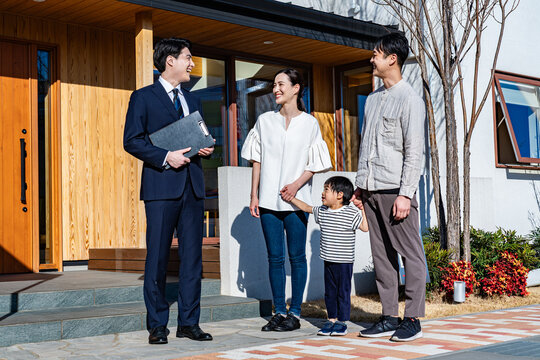 スーツの営業マンが家族（夫婦と子供）に新築住宅を案内しているシーン