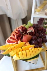 Fruit platter with pomegranate grapes grapefruit mango and mandarins on stand.