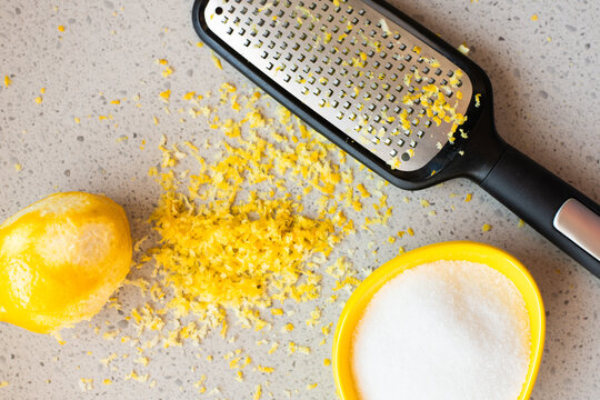 lemon is positioned next to grater with sugar and zest scattered