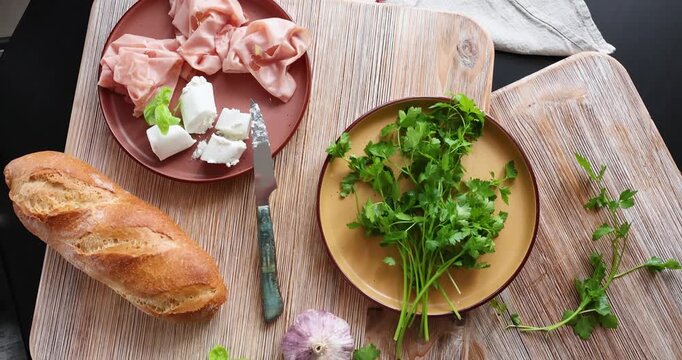 High-quality farm food on wooden cutting board. Top view. Flat lay photo. Soft goat cheese on bread, basil and mortadella sandwich. Italian tradition cuisine.