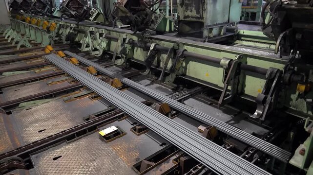 Industrial machines organize and secure long steel rebar rods into bundles within a metallurgy plant for efficient transport and distribution to construction sites and storage facilities.
