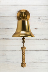 Vintage brass bell used on ships, with knotted rope, hanging on hook mounted to rustic wooden wall