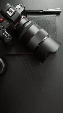Modern digital camera and lens set on a dark wooden surface with a pen
