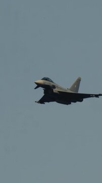 LUQA, MALTA - SEPTEMBER 28, 2025: Slow motion vertical shot of a German Air Force Eurofighter Typhoon fighter jet flying with landing gear down. The aircraft banks and passes by against a clear blue