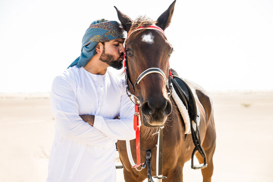 Young adult with Kandura, the emirates traditional clothes, riding his horse in the desert