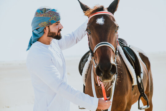 Young adult with Kandura, the emirates traditional clothes, riding his horse in the desert