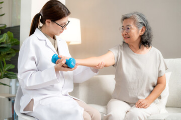 Fototapeta premium Asian physiotherapist helping senior patient with dumbbell exercise, doctor therapy rehabilitation for arm strength, muscle recovery and mobility support, homecare service, caregiver support elderly.