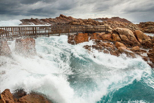 Huge waves crashing under a bridge linking coastal rock formations