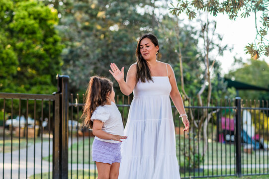 A woman and a girl stand in front a park with trees around them, enjoying their time together.