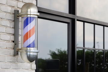 Barber pole spinning on white brick of barber shop background.