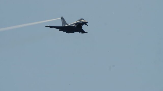 LUQA, MALTA - SEPTEMBER 28, 2025: A military Eurofighter Typhoon jet soars through the sky, performing a high-speed pass. The clip follows the aircraft as it leaves a white wingtip vapor trail and