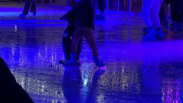 Young person learning to ice skate using a fun penguin helper on a vibrant blue-lit rink, promoting joyous winter leisure and holiday season recreation activity